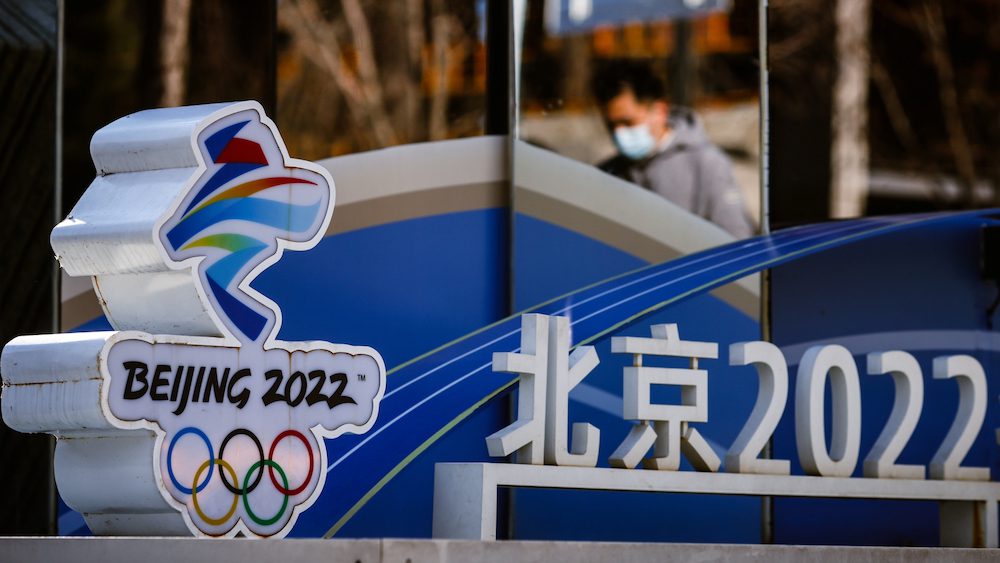 A man is reflected in a mirror as he walks past the logo of the Beijing 2022 Olympics in Beijing